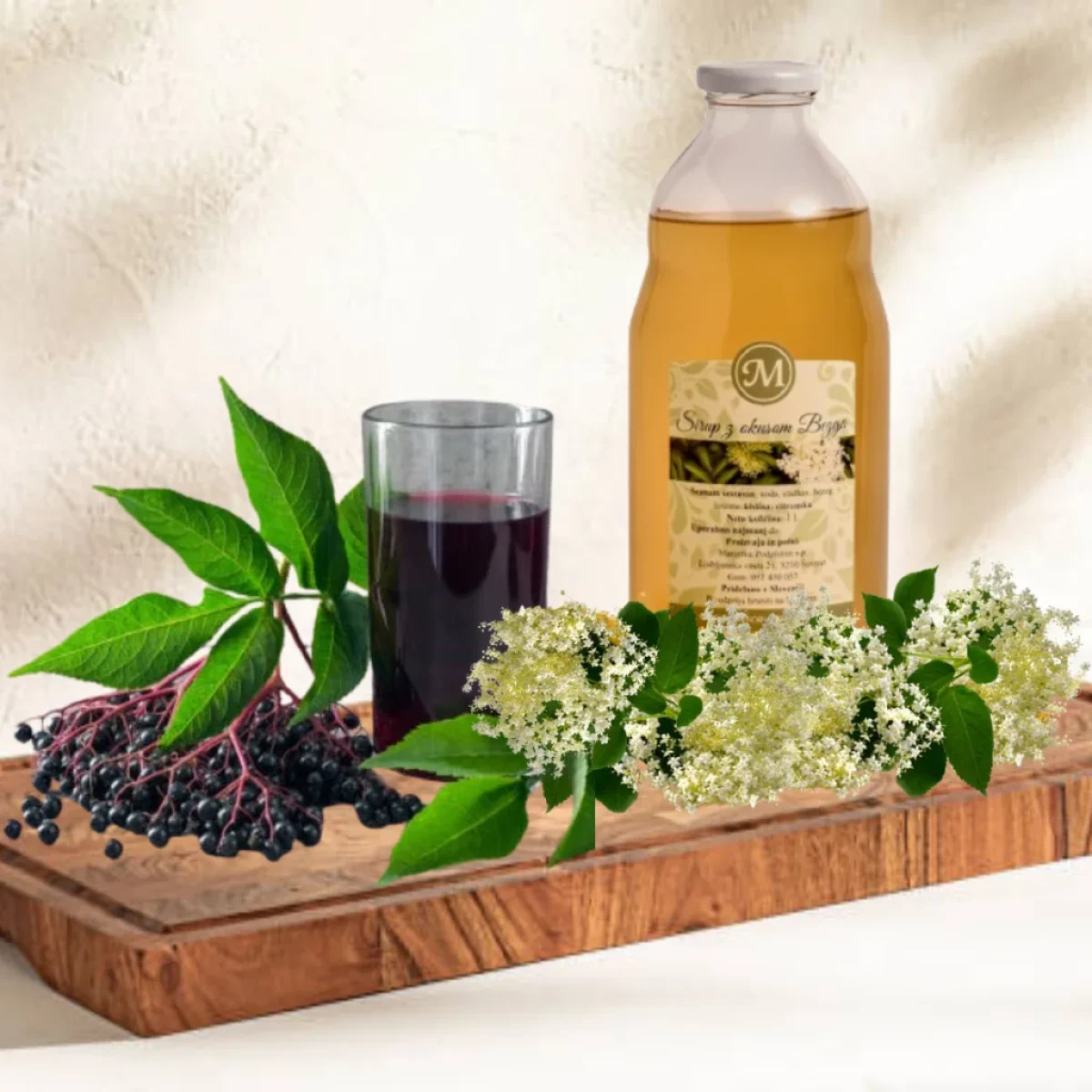 Kozarec bezgovega soka in steklenica bezgovega sirupa na lesenem podstavku, pripravljeno za pitje