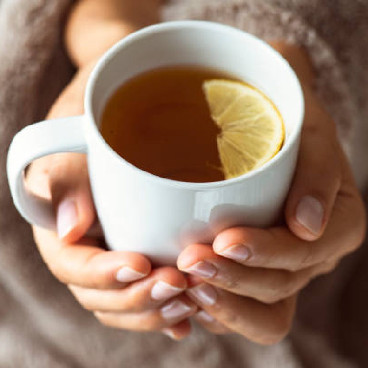 Roke držijo skodelico z zeliščnim čajem – trenutek umirjenosti in prisotnosti